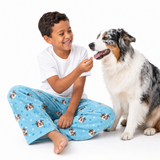 Light blue paws theme – child in dog-print pajamas offering treat to multicolored dog.