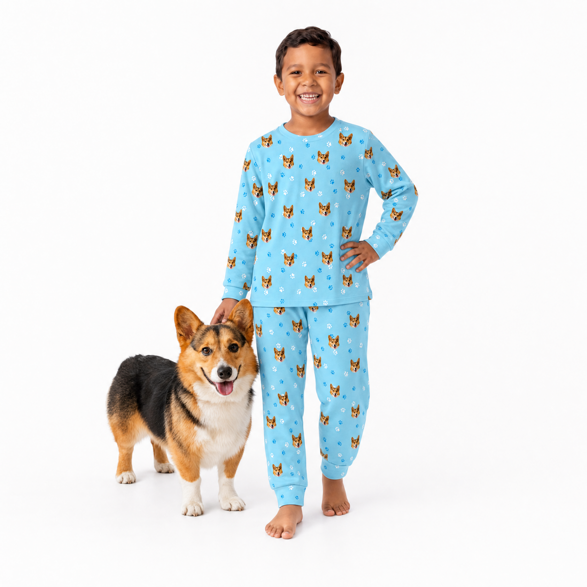 Child wearing light blue jogger pajamas with dog pattern standing next to a dog on a white background