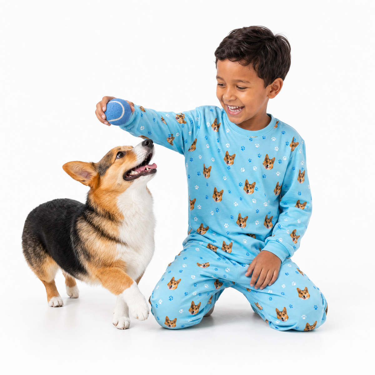 Child in light blue jogger pajamas with dog pattern playing with a dog on a white background
