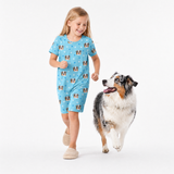 Girl in a light blue nightgown with dog pattern walking a dog on a white background