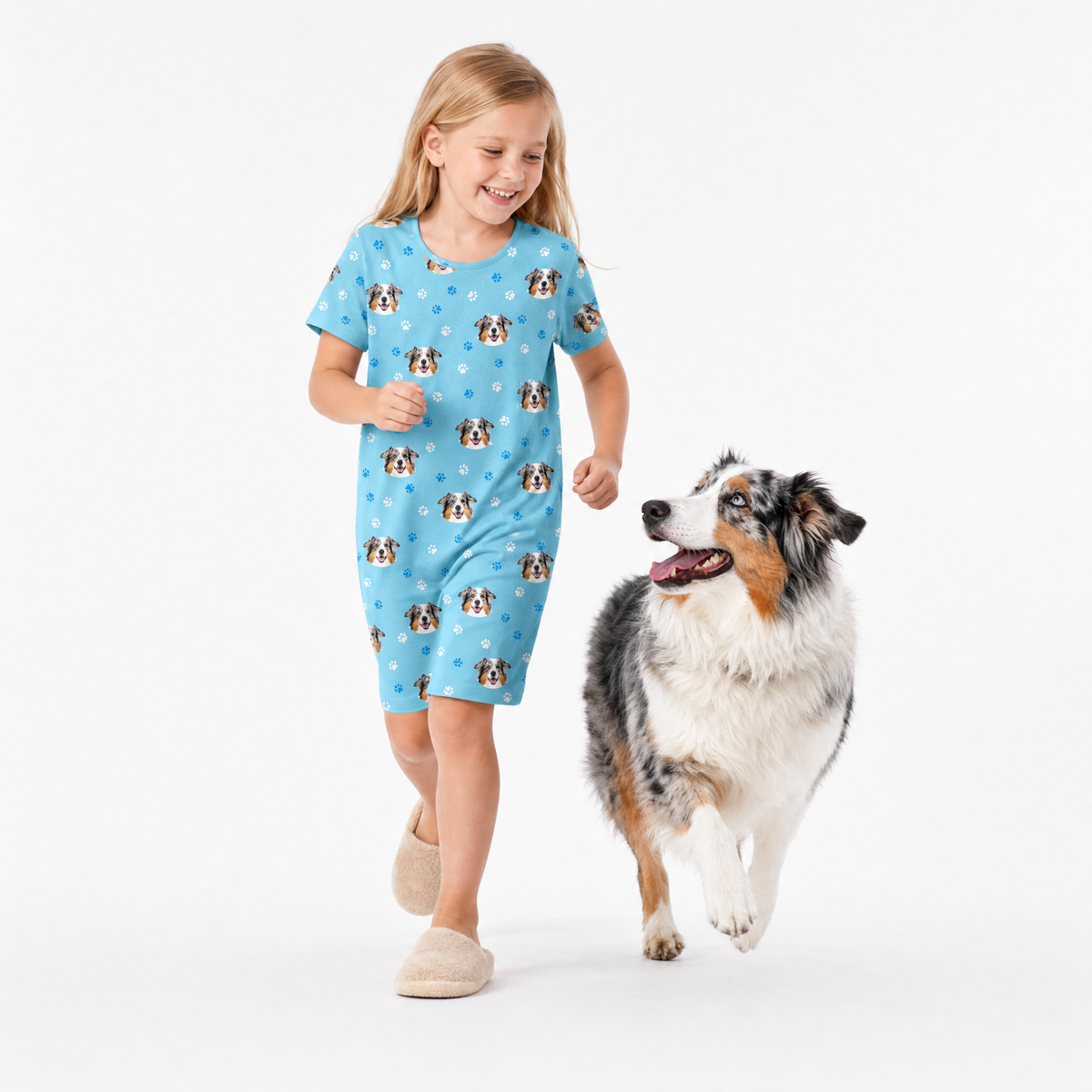 Girl in a light blue nightgown with dog pattern walking a dog on a white background