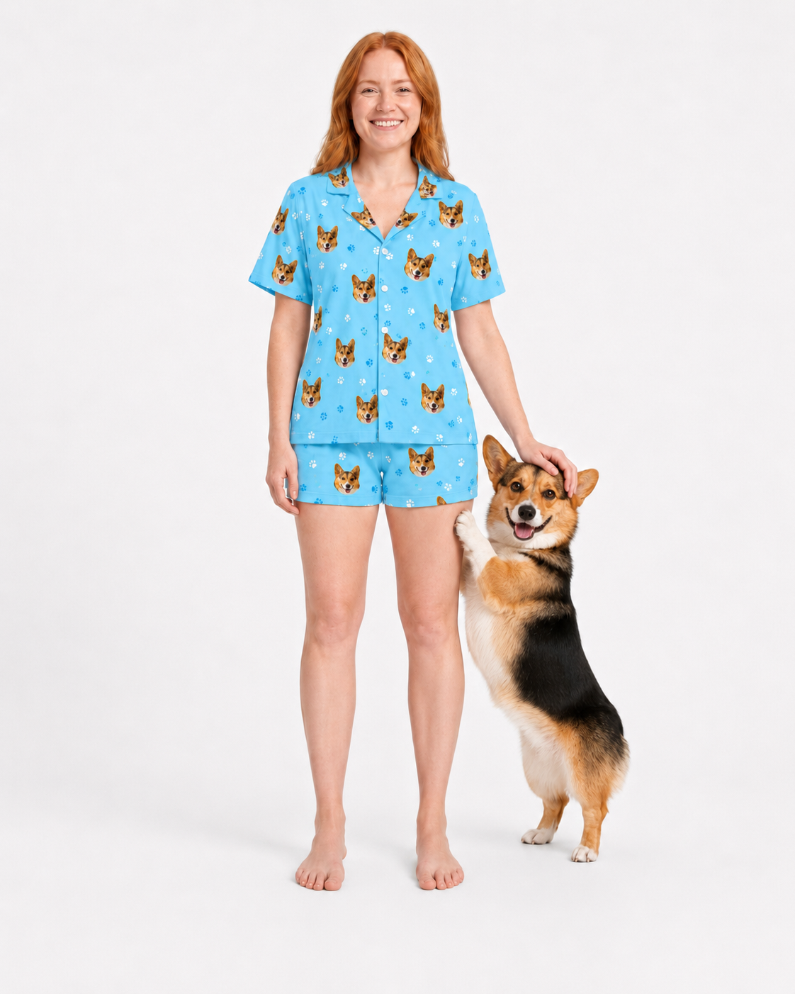 Woman wearing a light blue paws pajama set with dog pattern, standing next to a dog on a white background
