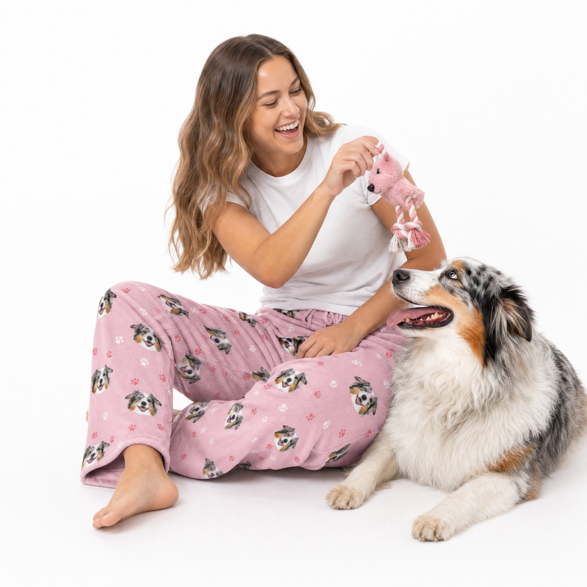 Woman in pink pajama pants with dog pattern sitting next to a dog on a white background