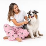 Light pink paws theme – person in dog-print pajamas brushing fluffy dog.