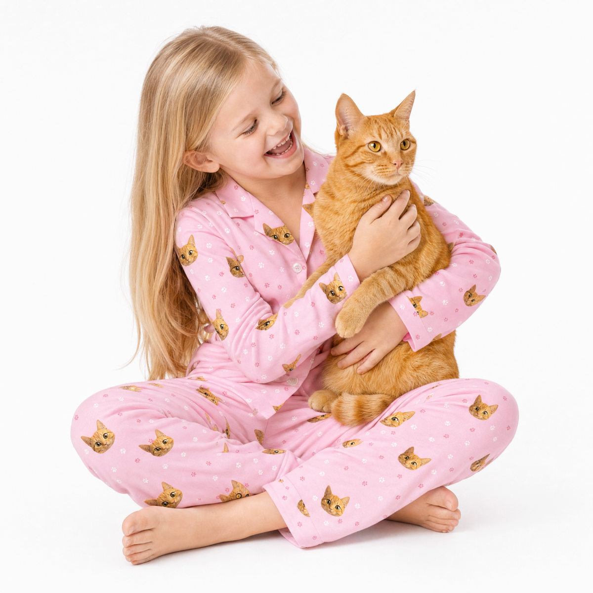 Girl in pink pajamas with cat pattern holding an orange cat on a white background