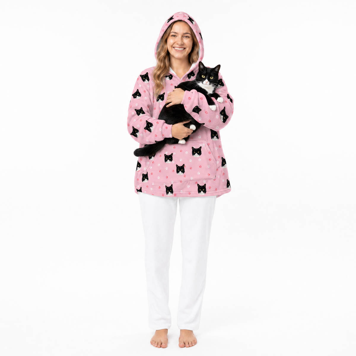 Person wearing a pink blanket hoodie with black cat patterns, holding a black cat on a white background