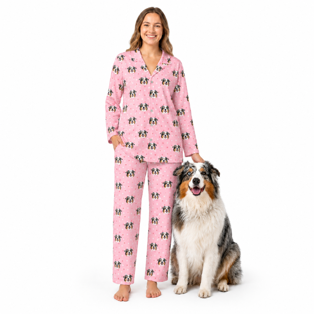 Woman wearing light pink paws pajamas with dog pattern standing next to a dog on a white background