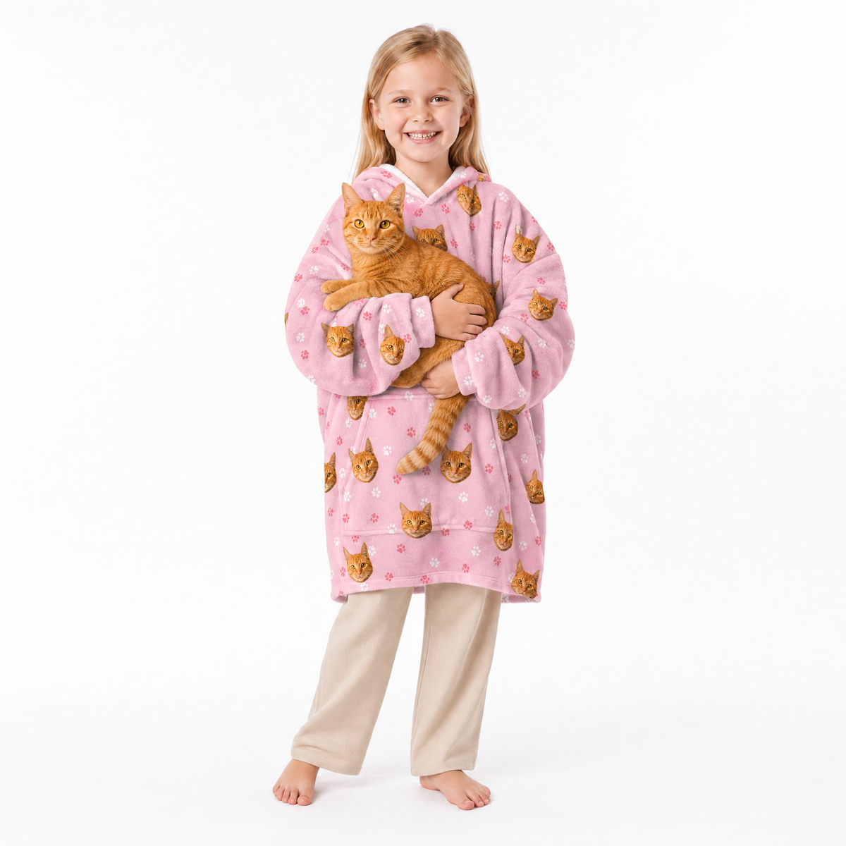 Child wearing a pink blanket hoodie with cat prints, holding an orange cat on a white background