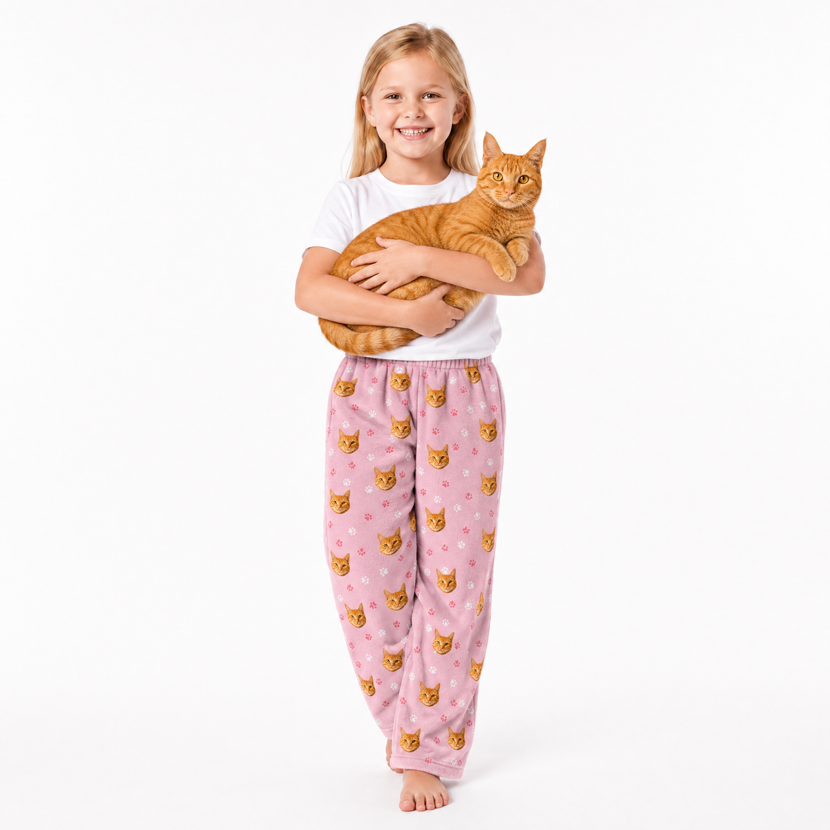 Child wearing pink cat-themed pajama pants holding an orange cat on a white background
