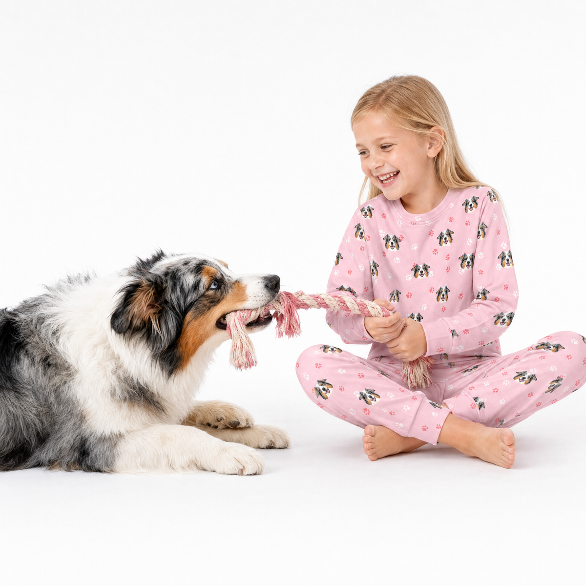 Girl in pink jogger pajamas playing with a dog on a white background