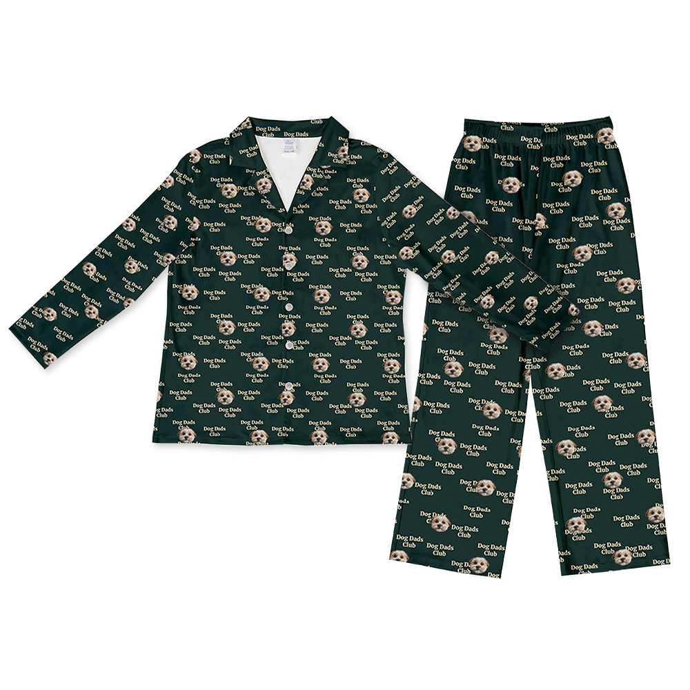 A matching set of long-sleeve, button-down pajama top and loose-fit pajama bottoms, in a dark green fabric. The entire set is covered in a repeating pattern featuring alternating elements: the phrase "Dog Dads Club" in text, and smiling headshots of a dog.