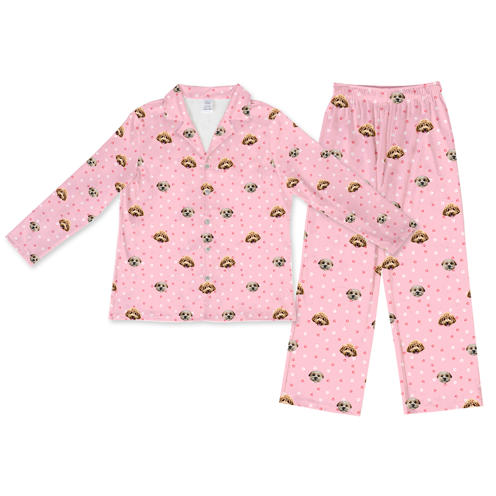 A two-piece pajama set, consisting of a long-sleeved, button-down top and matching long pajama pants with an elastic waist. Both pieces are light pink and feature a repeated pattern of two different dog faces.