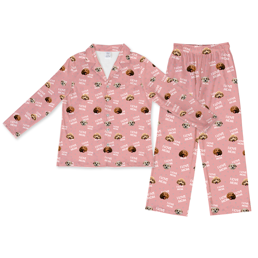 A pink long-sleeve pajama set, consisting of a button-down top and matching full-length pants. Both pieces feature a repeating pattern of various dog faces in different shades of brown and white, and white text reading "I LOVE MOM" interspersed with small white hearts.
