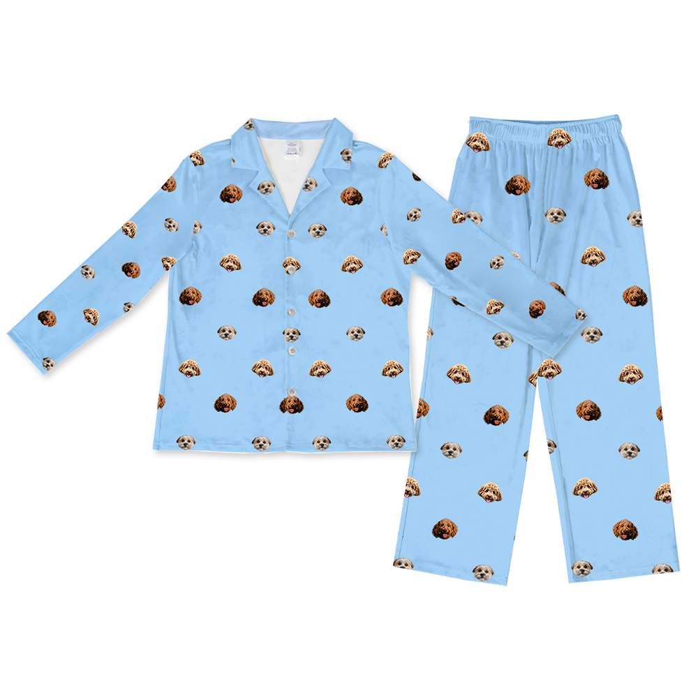 A two-piece pajama set, consisting of a long-sleeved, button-down top and matching long pajama pants with an elastic waist. Both pieces are sky blue and feature a repeated, scattered pattern of three different dog faces.