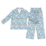 A two-piece children's pajama set featuring a light blue long-sleeve button-front top and matching pants, both printed with a repeating pattern of white dogs, snowmen, pine trees, and clouds.