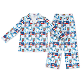 A two-piece children's pajama set featuring a long-sleeve button-up top and matching pants, both printed with a collage pattern of cartoon dogs in winter outfits on a light blue and white background.