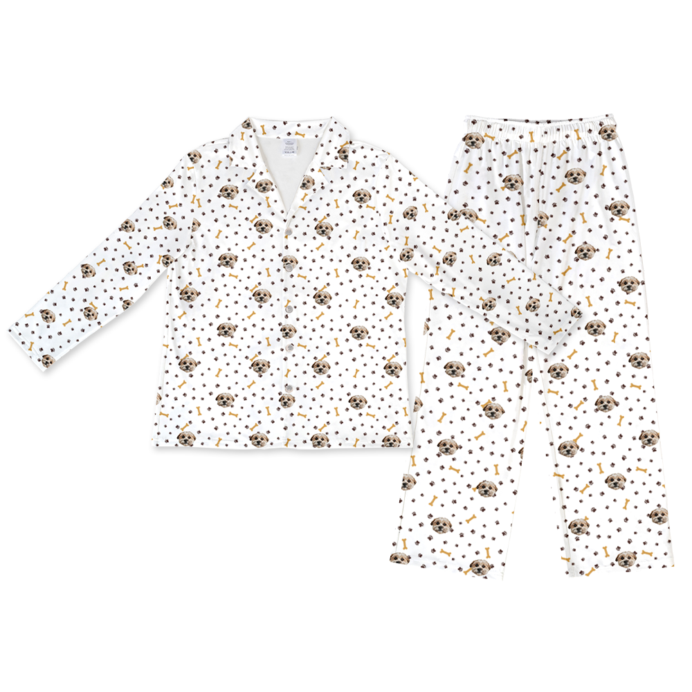White long-sleeve pajama set, including a button-down top and full-length pants, both featuring a scattered pattern of dog faces, brown paw prints, and yellow-brown dog bones.