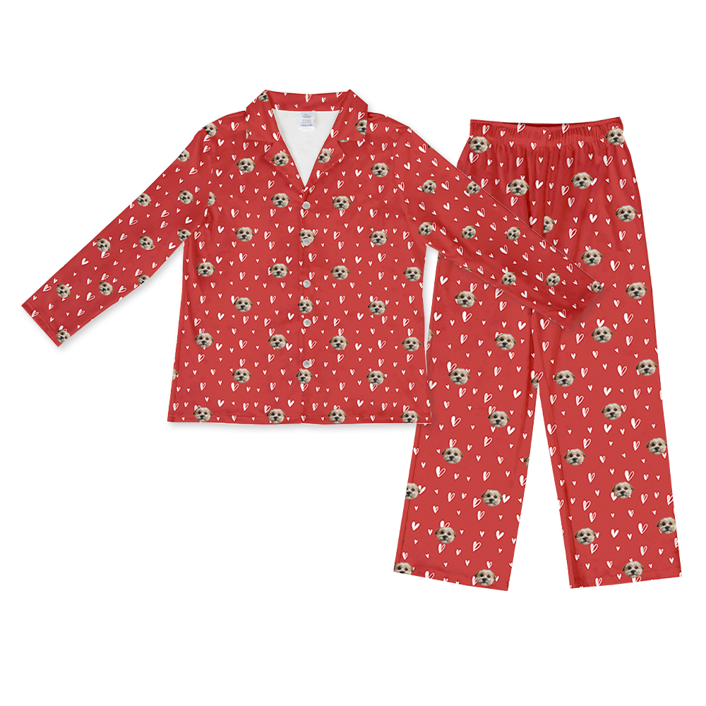Matching long-sleeve red pajama set with a button-down top and pants, featuring a repeating pattern of white hearts and the custom face of one light-colored dog.
