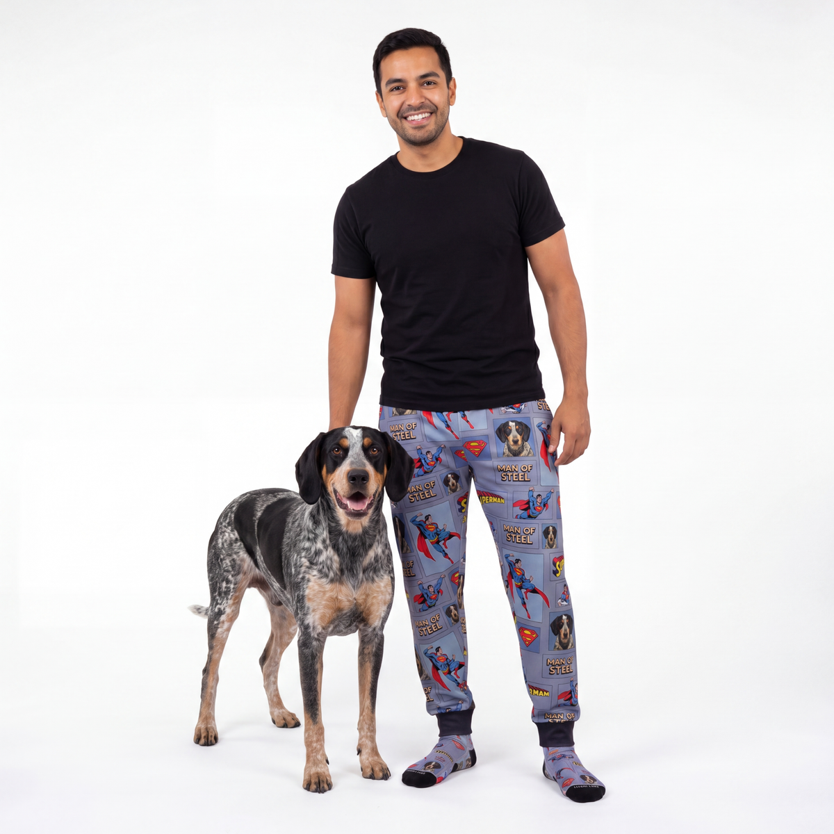Man wearing superman pajama pants standing next to a dog on a white background