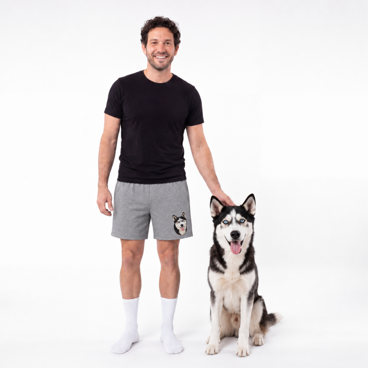 Man wearing black t-shirt and gray shorts with a dog on a white background