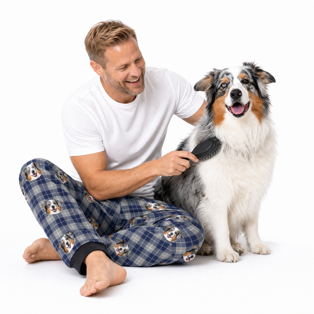 Man brushing a dog while wearing pajama pants with a dog pattern on a white background