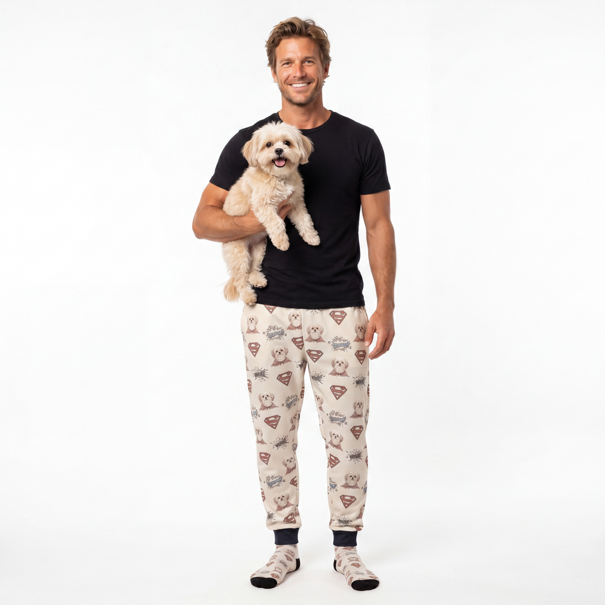 Man wearing superman pajama sweatpants with a dog pattern, holding a small dog on a white background