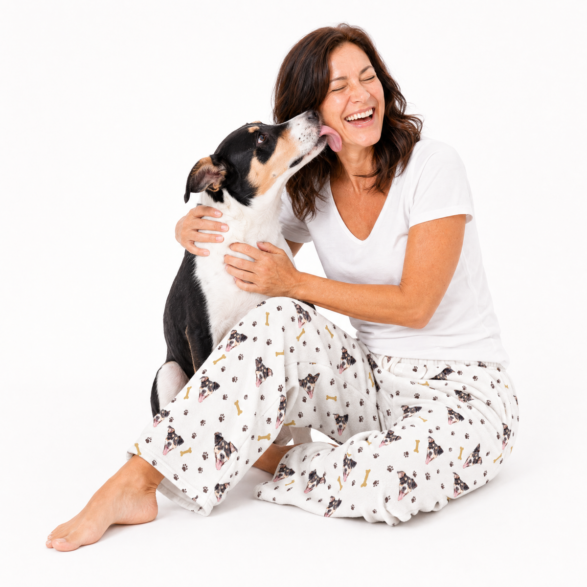 Woman in pajama pants with dog pattern sitting on the floor with a dog.