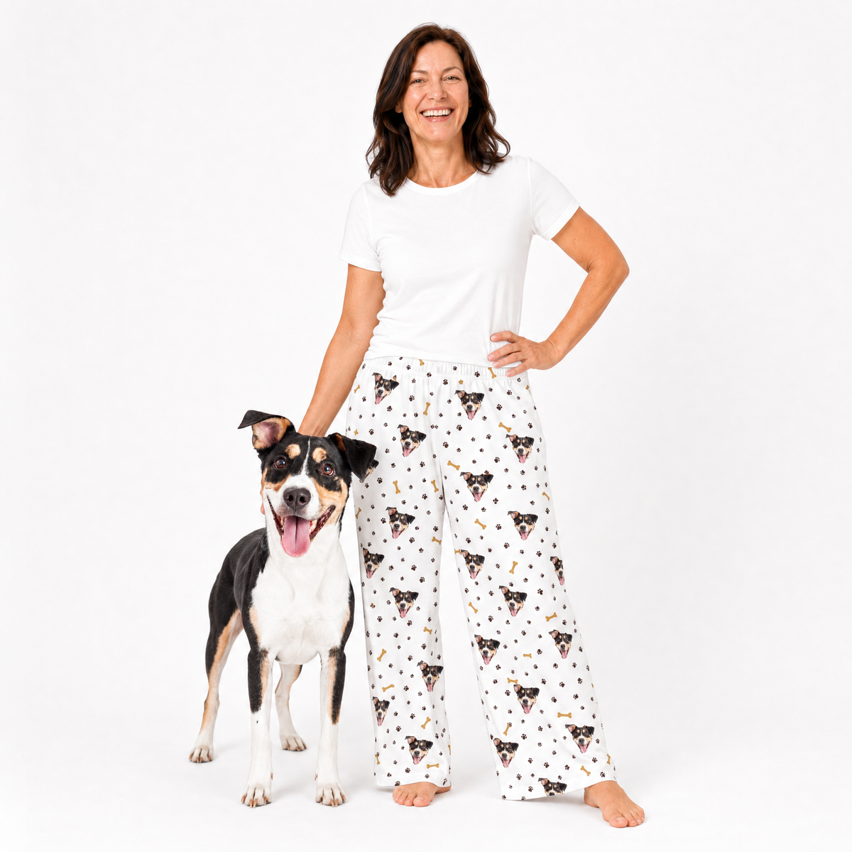 Woman wearing a white t-shirt and patterned pajama pants with a dog standing next to her on a white background