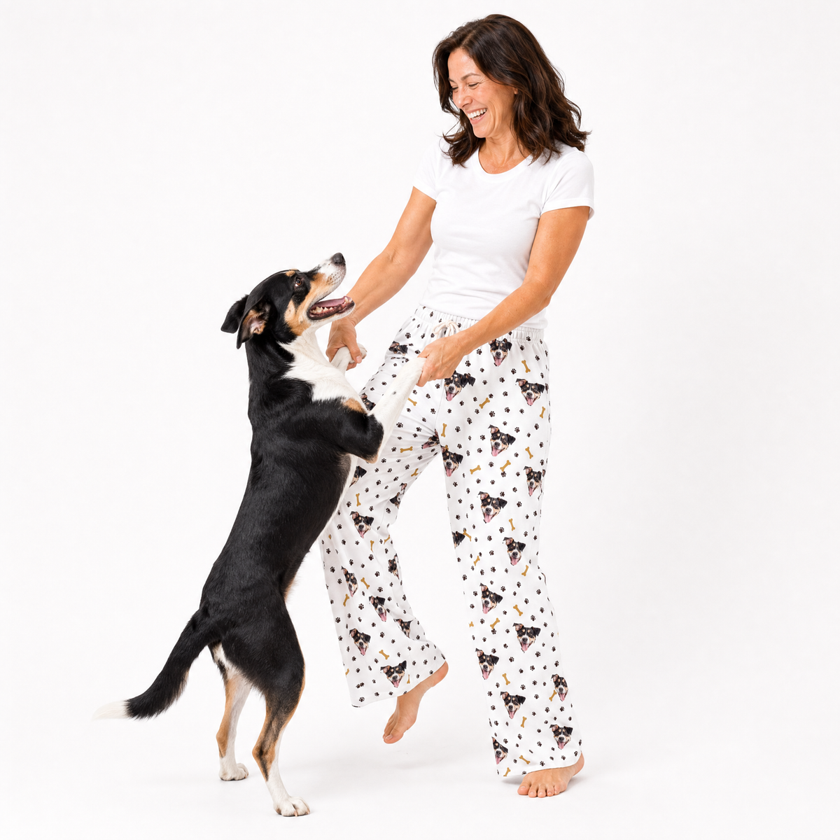 Paws and bones theme – person in dog-print pajamas playing with black, white, and tan dog.