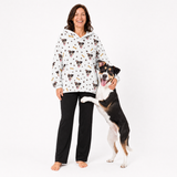 Woman wearing a white blanket hoodie with dog pattern and a dog standing next to her on a white background
