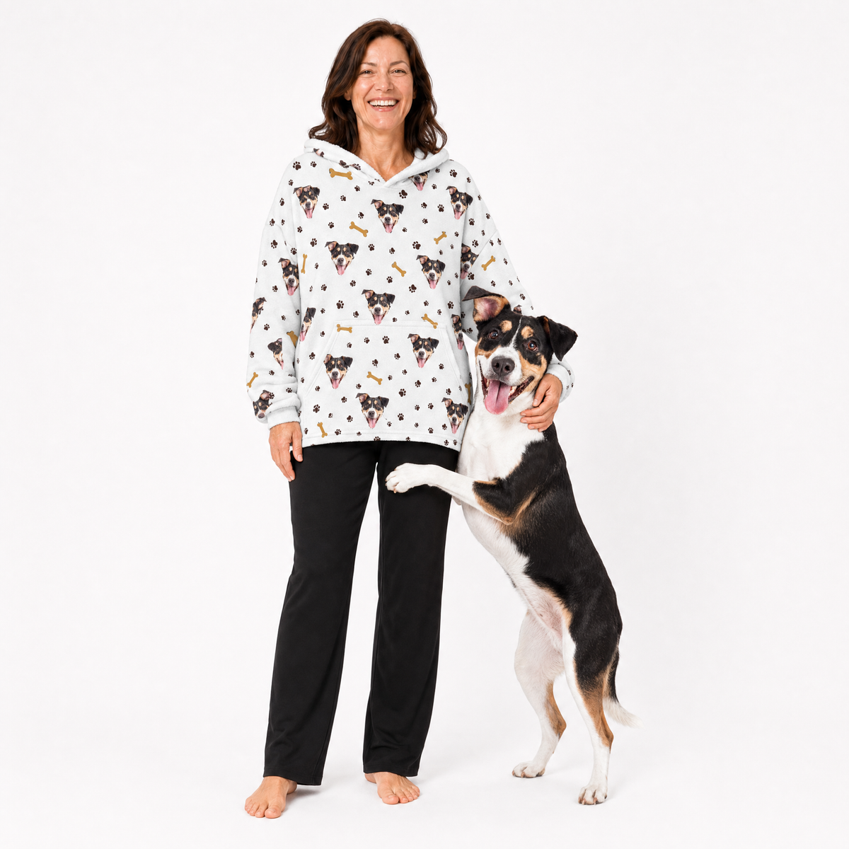 Woman wearing a white blanket hoodie with dog pattern and a dog standing next to her on a white background