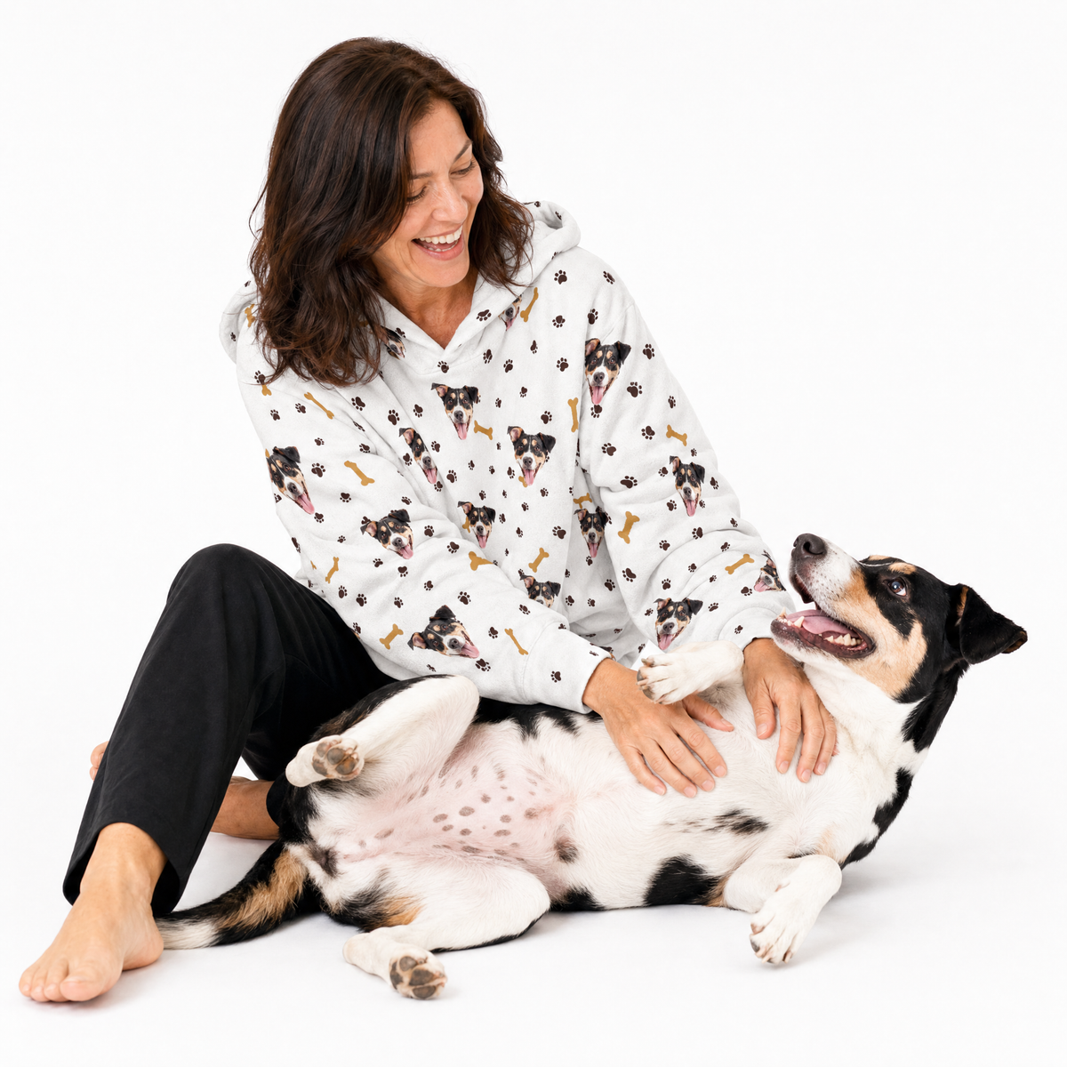 Woman wearing a white patterned blanket hoodie sitting with a large dog on a white background