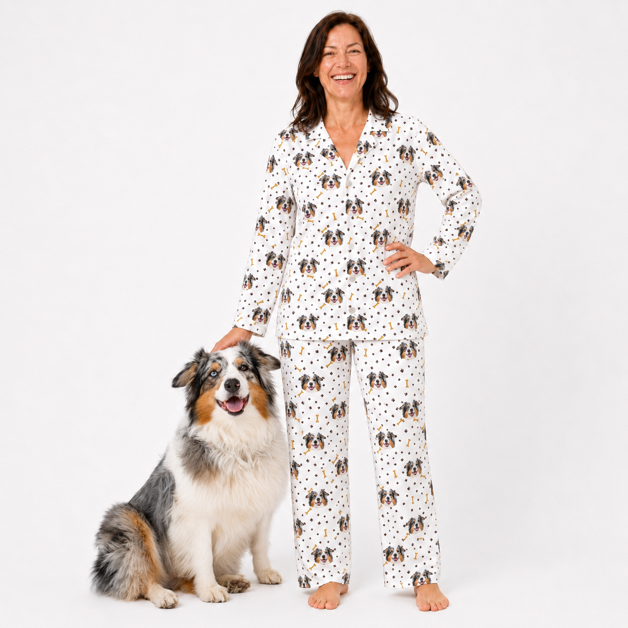 Woman wearing a pajama set with dog pattern standing next to a dog on a white background