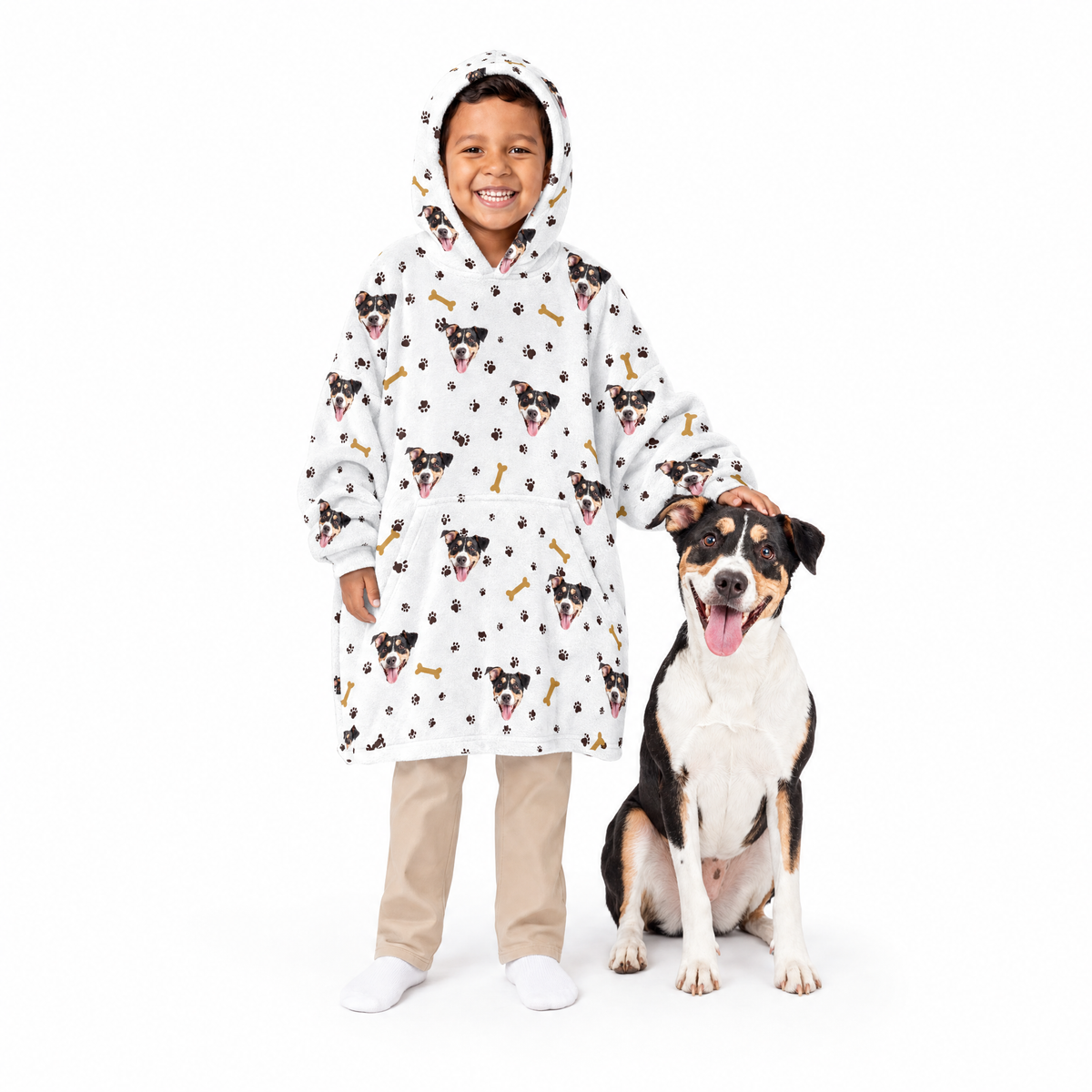 Child wearing a white blanket hoodie with dog pattern standing next to a dog on a white background