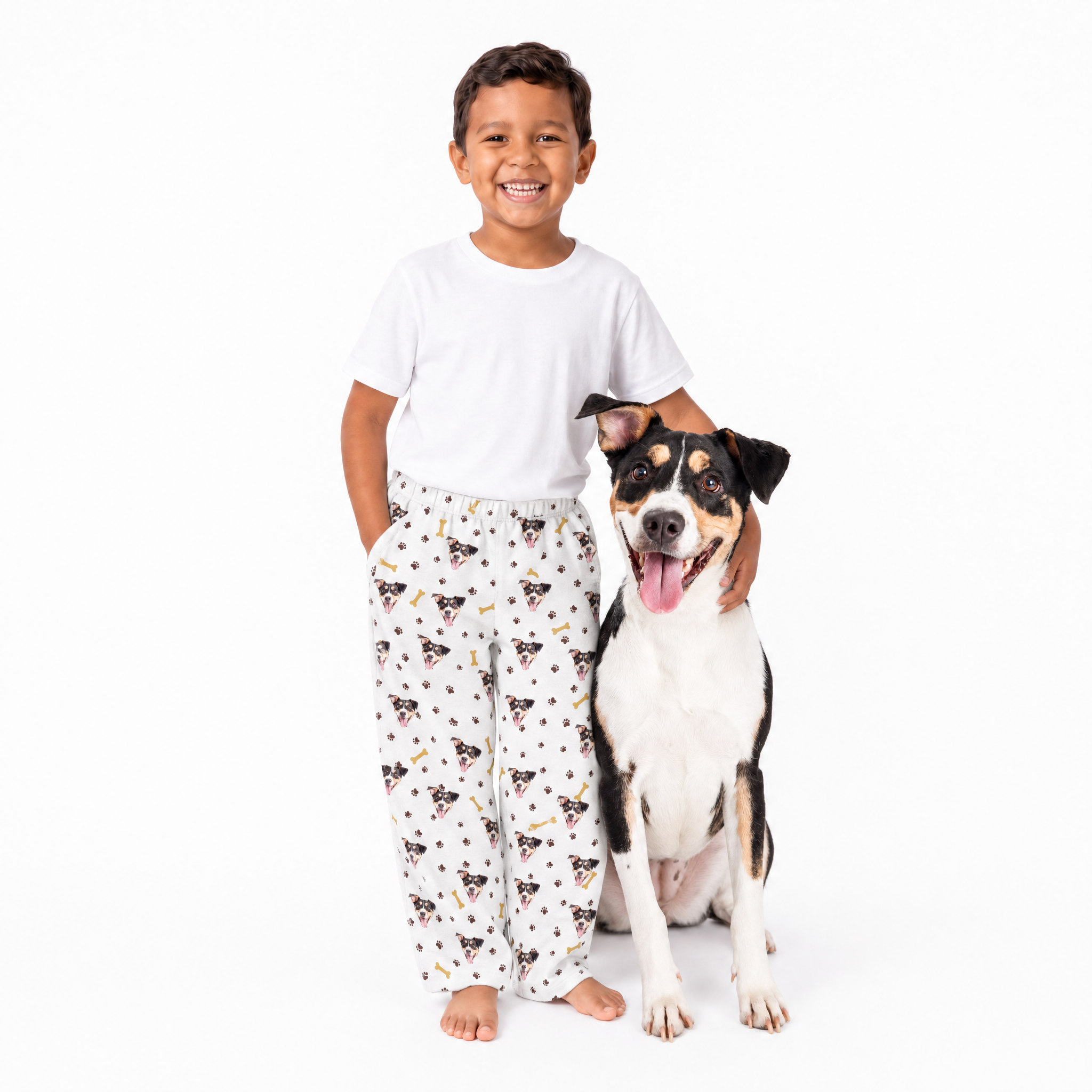 Child wearing pajama pants with dog pattern standing next to a dog on a white background