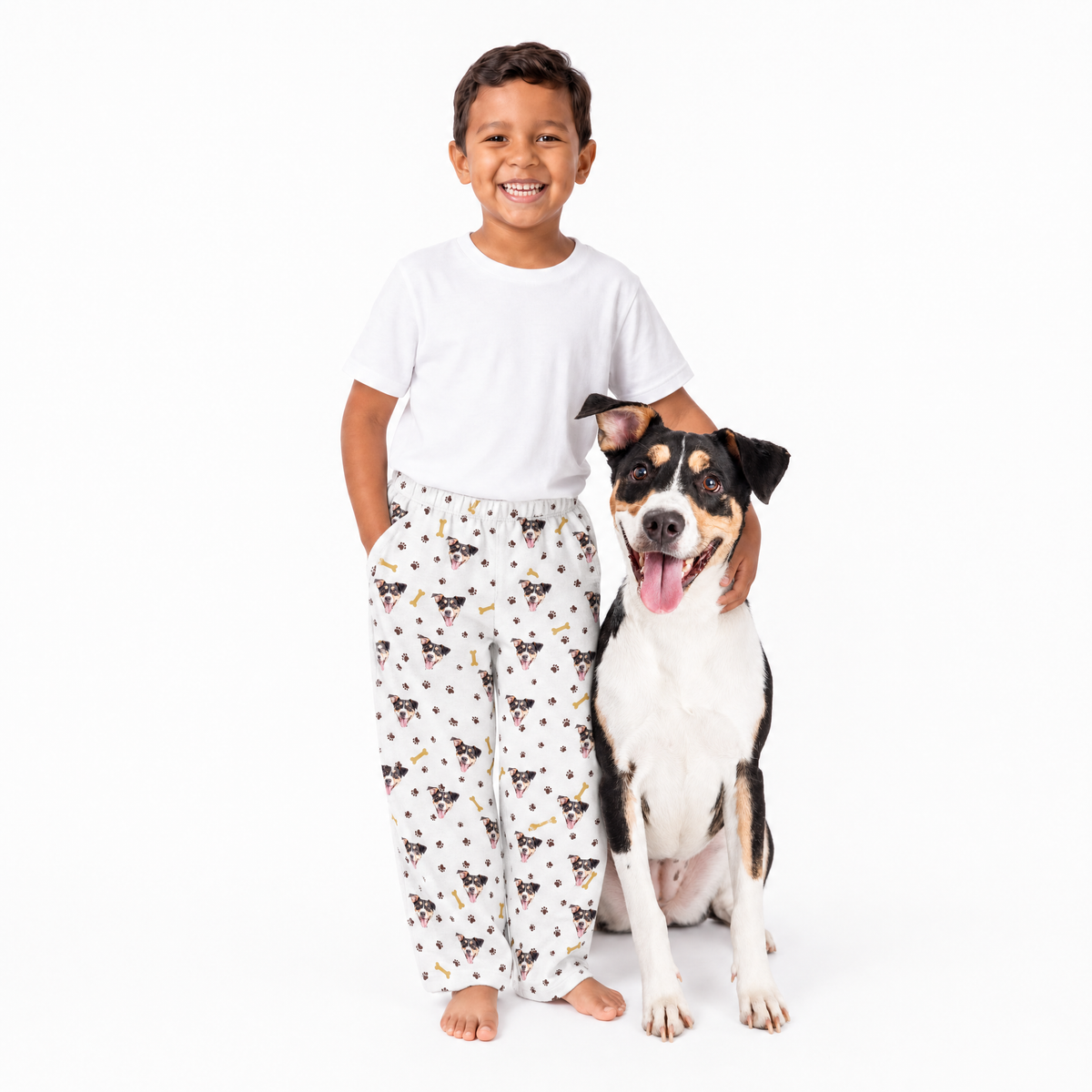 Child wearing pajama pants with dog pattern standing next to a dog on a white background