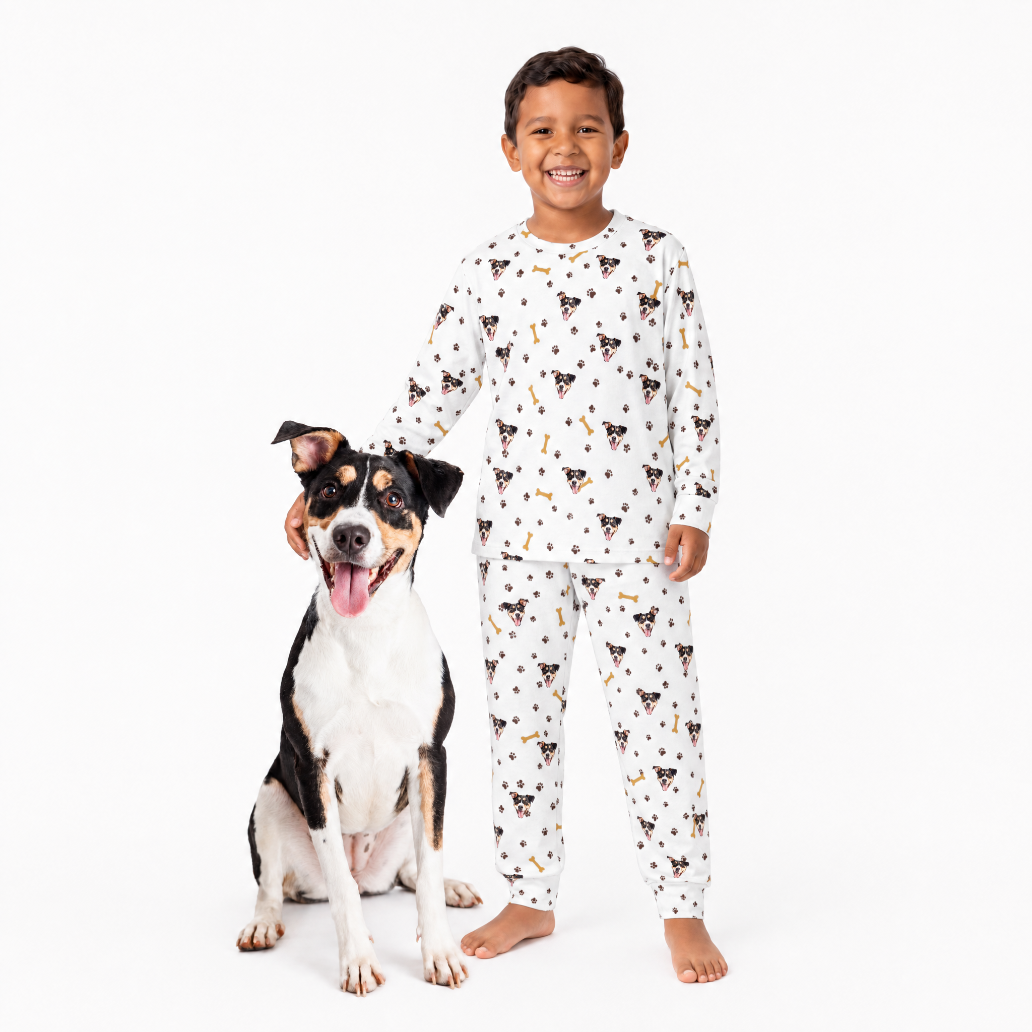Child wearing a white jogger pajama set with dog pattern standing next to a dog on a white background