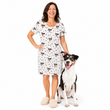 Woman wearing a dog patterned nightgown standing next to a dog on a white background