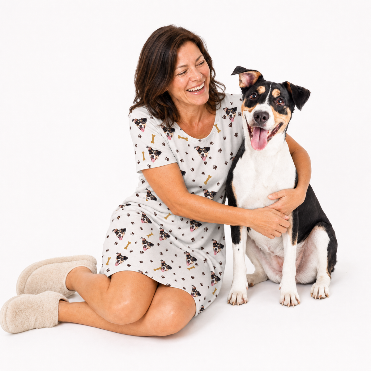 Woman wearing a dog patterned nightgown sitting with a dog on a white background
