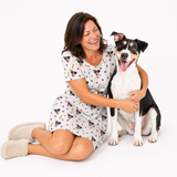 Woman wearing a dog patterned nightgown sitting with a dog on a white background