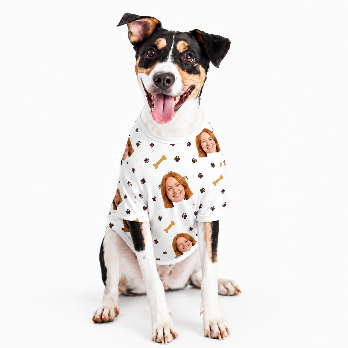 Dog wearing a white custom dog shirt with a repeating face, paw print, and bone pattern on a white studio background.