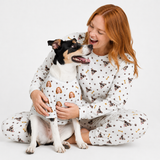 Woman and dog wearing matching white custom pet pajamas with a repeating dog face, paw print, and bone pattern.