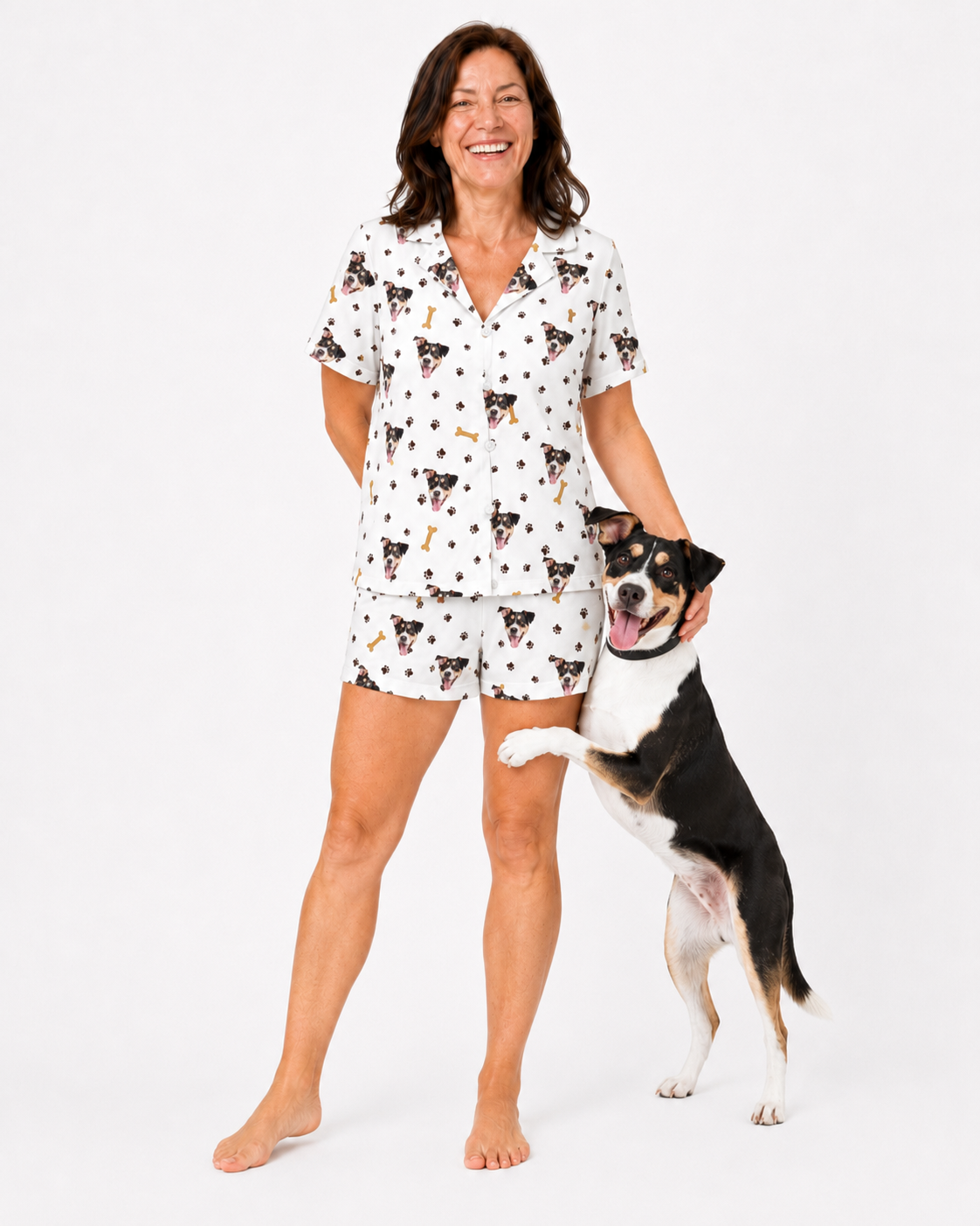 Woman wearing a dog-patterned pajama set standing next to a dog on a white background