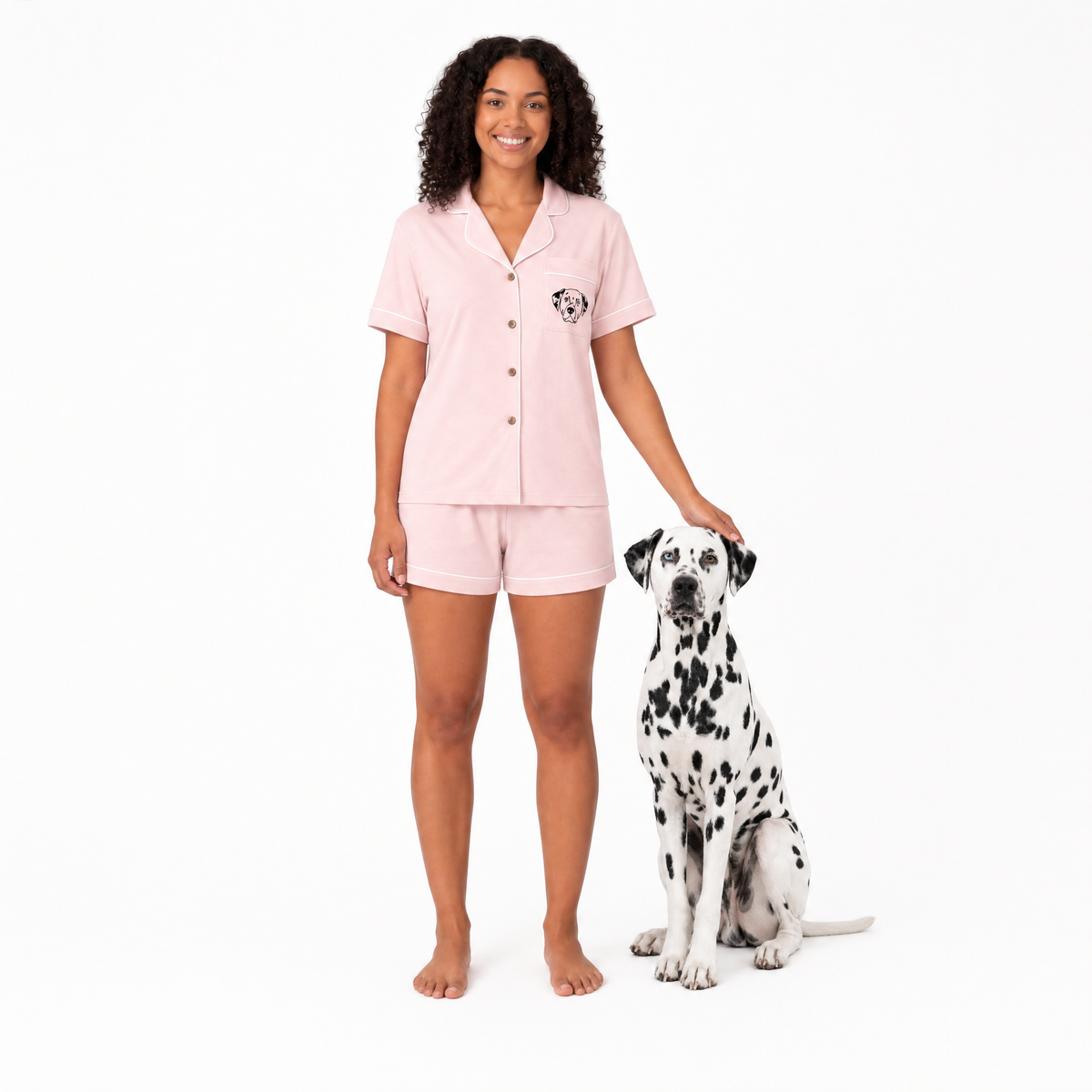 Woman wearing pink pajamas standing next to a Dalmatian dog on a white background