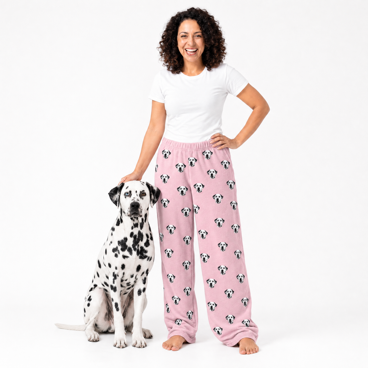 Woman wearing pink pajama pants with dog pattern standing next to a Dalmatian dog on a white background