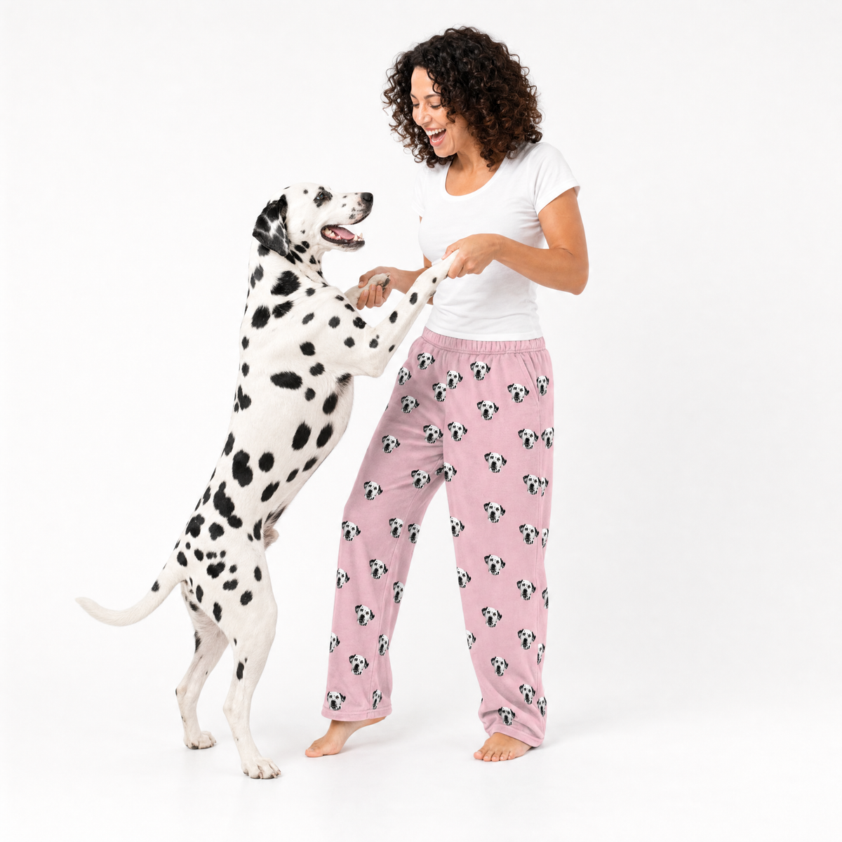 Woman wearing pink pajama pants with dog pattern standing next to a Dalmatian dog on a white background
