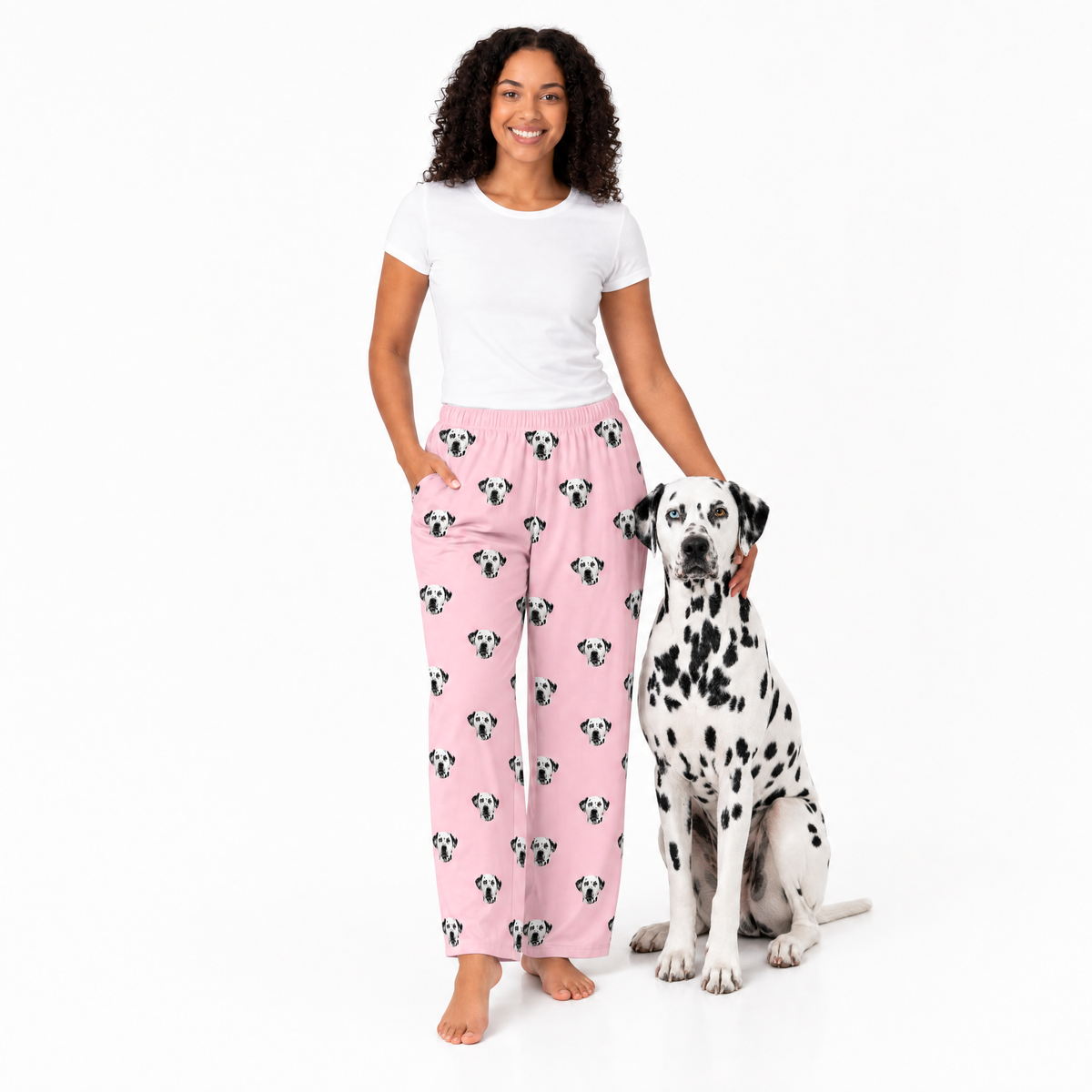 Woman wearing pink pajama pants with dog pattern and a Dalmatian dog on a white background