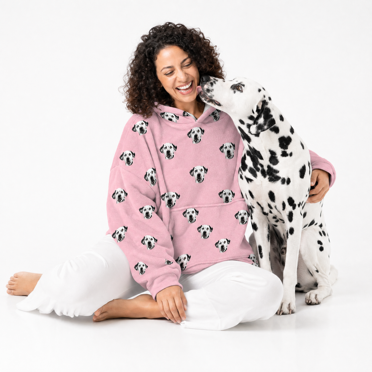 Woman wearing a pink blanket hoodie with Dalmatian pattern sitting on the floor with a Dalmatian dog.