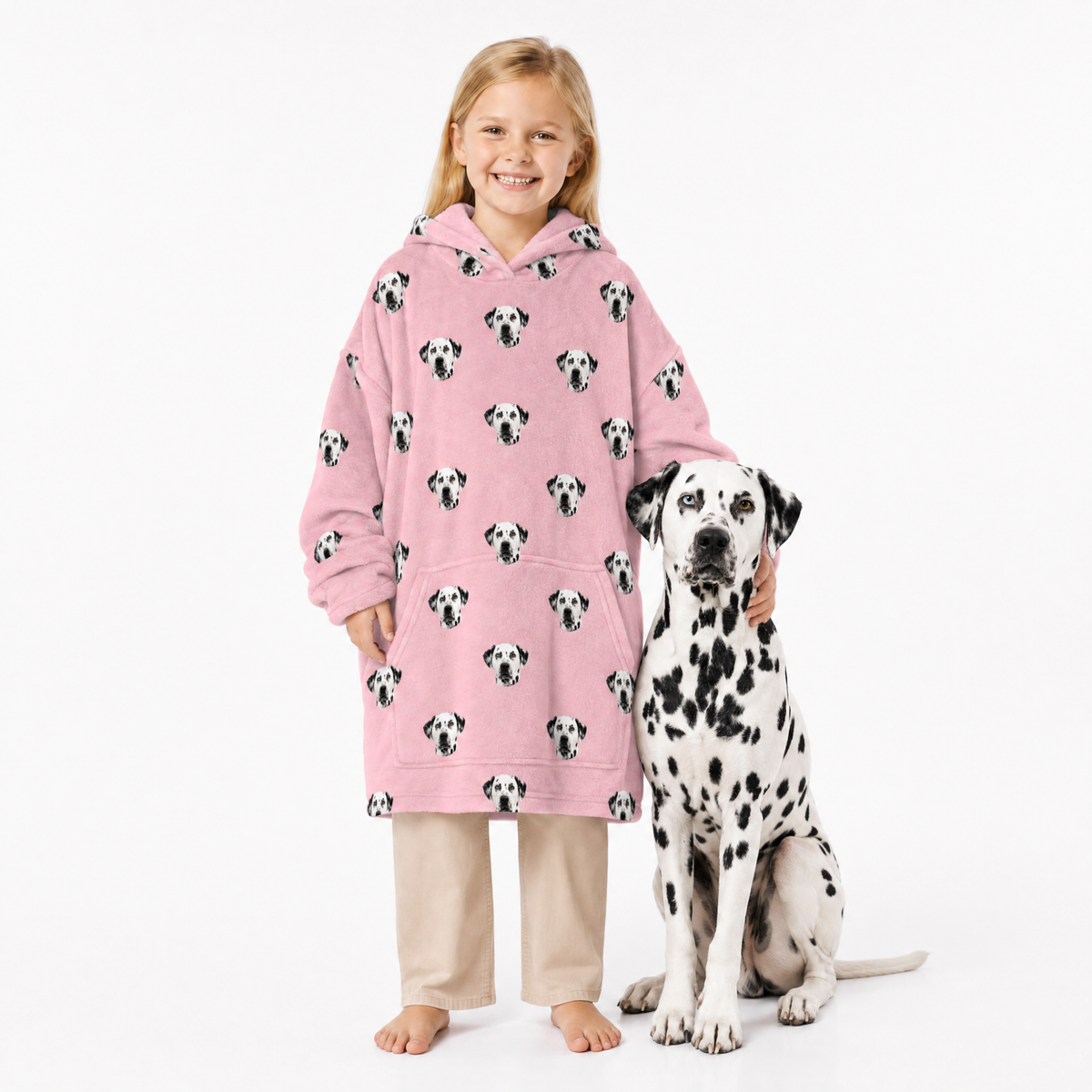 Child wearing a pink blanket hoodie with Dalmatian pattern standing next to a Dalmatian dog on a white background