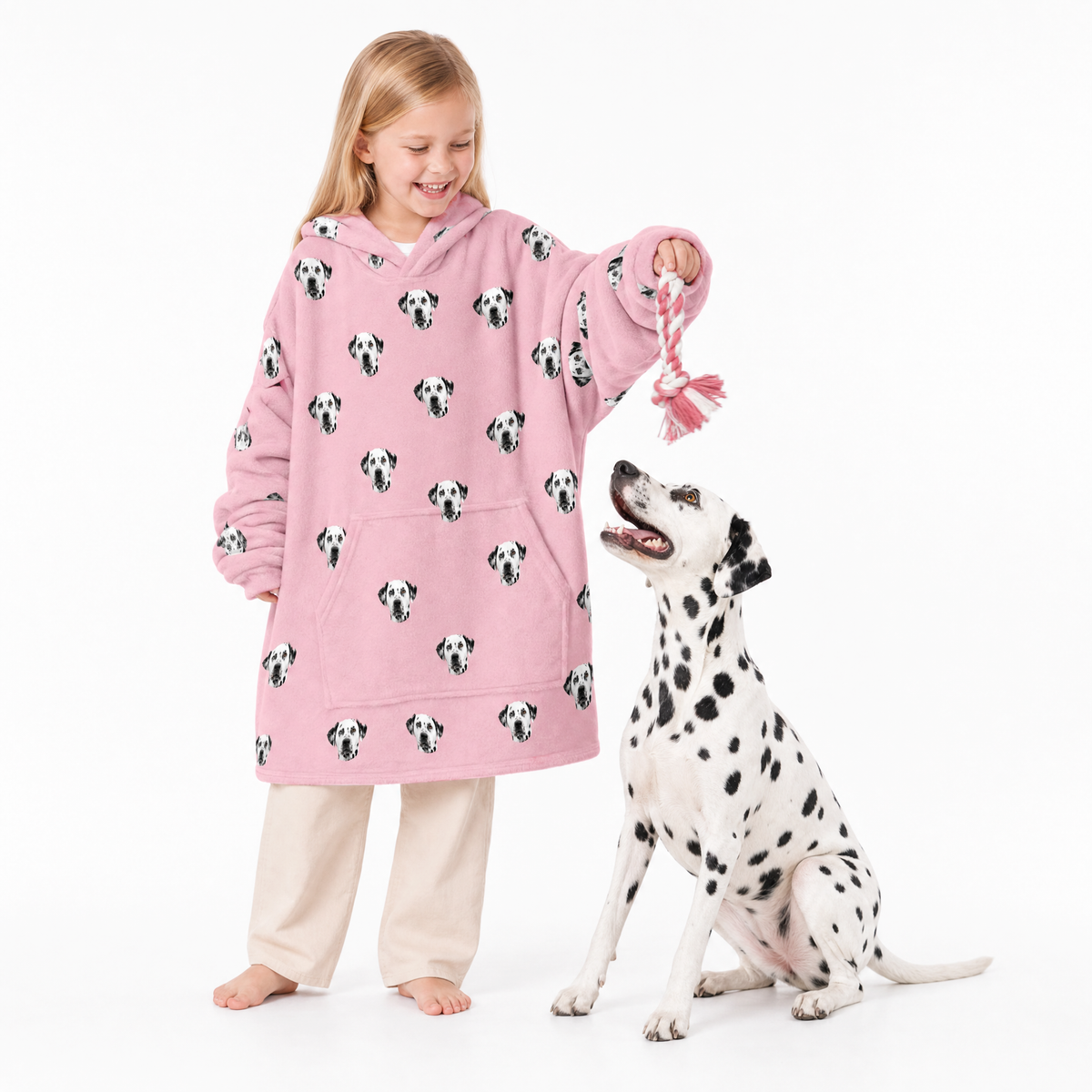 Girl in pink Dalmatian-patterned blanket hoodie and pants standing next to a Dalmatian dog on a white background